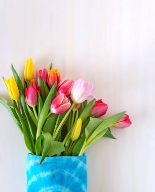 Beyaz bulanık arkaplanda dokuma bir çantada çok renkli laleler.