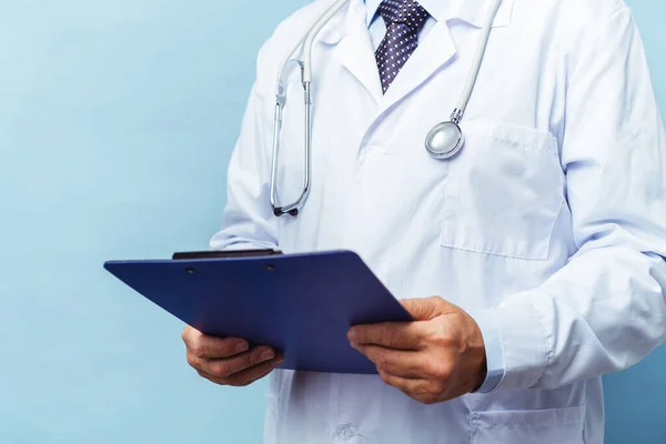 Een arts met een stethoscoop. Op een blauwe achtergrond. De dokter houdt de map in zijn handen en maakt een afspraak in de kliniek. Concept ziektepreventie — Stockfoto