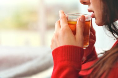 Genç bir kadın limonlu çayla elinde fincanla rahatlıyor. Kız pencereden dışarı bakıyor. Evde limonlu çay içerken düşünen genç bir kadın..