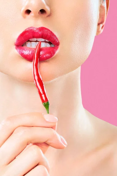 Young woman with chili red pepper isolated en pinc background. Sexy female lips. Hot seductive girl