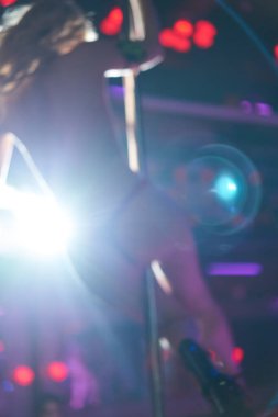 Görüntü bulanık. Gece kulübünde direkli striptiz yapan genç seksi kadın. Sahnede güzel çıplak striptizci kız. Yüksek topuklu ayakkabıyla güzel kadın bacakları.