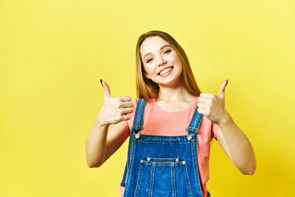 Blij opgewonden vrouw glimlach houdt duimen omhoog gebaar, mooie jonge vrouw glimlach kijkt naar de camera. geïsoleerde ob gele backgroud. — Stockfoto