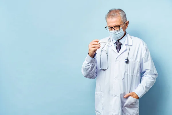 Portrait of a handsome senior doctor holding a thermometer in his hands, on a thermometer, the normal temperature of a healthy person is 36.6 degrees Celsius. Healthcare concept, flu prevention. — Stock Photo, Image