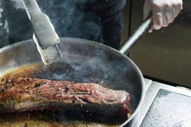 Şef restoranın mutfağında çalışıyor. Büyük bir tavada kızartılmış taze et. Restoran mutfağı geçmişi
