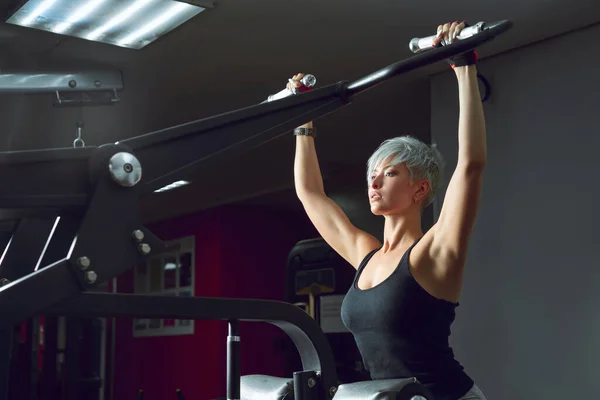 Sportovní žena čerpající svaly na simulátoru ve fitness centru — Stock fotografie