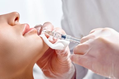 Bir kozmetoloji salonunda dudak şekli düzeltme prosedürü. Uzman, hastanın dudaklarına bir iğne yapar. Dudak büyütme