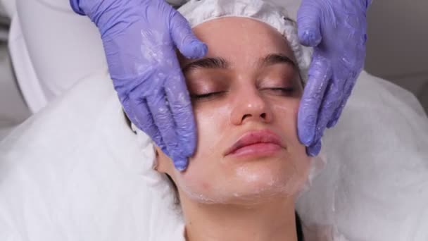 Косметическая процедура. Массаж лица, женщина в салоне красоты с маской на лице. Применение маски . — стоковое видео