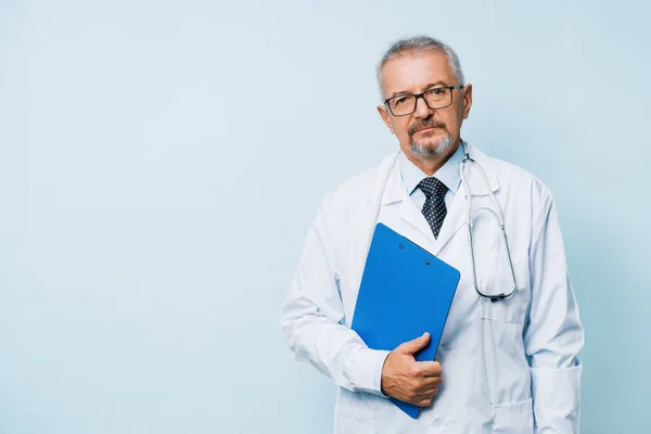 Elderly bearded male doctor in white uniform with a stethoscope with a blue folder. Doctor on the background of a medical research laboratory. — Stock Photo, Image