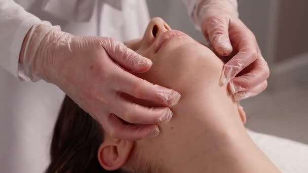 Ung kvinna på hälsosam massage behandling i kosmetologi spa center. Massageterapeut gör manuell buckalmassage på klienter ansikte, sida visa. — Stockvideo