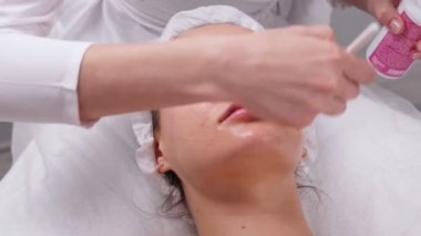 Kozmetik uzmanı kadın yüzüne, boynuna ve göğsüne güzellik kliniğinde fırça kullanarak maske takıyor. Cilt bakımı yapan bir güzellik uzmanı. Doktorların elleri ve hastaların yüzleri. Kozmetolojide kaplıca.