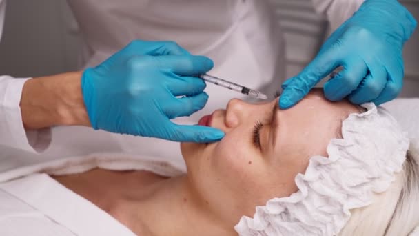 El médico cosmetólogo realiza el procedimiento de inyecciones faciales rejuvenecedoras para apretar y alisar las arrugas en la piel de la cara de una hermosa mujer joven en un salón de belleza.. — Vídeo de stock