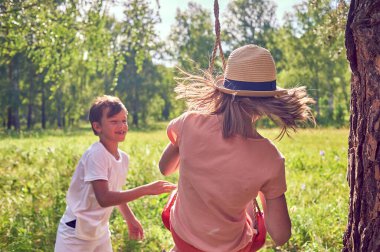 Çocuklar doğada oynar ve güler. Bir oğlan salıncakta bir kızı sallıyor. Yaşam tarzı fotoğrafı.
