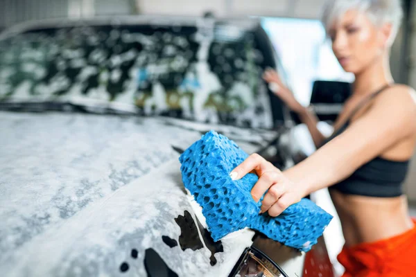 Sexy young woman washes a car in a car wash