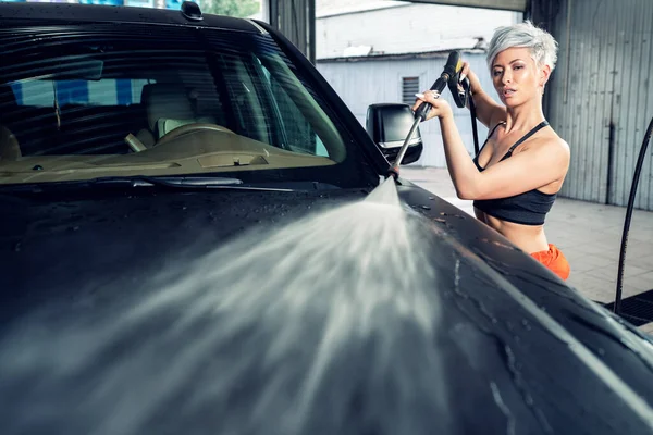 Sexy młoda kobieta myje a samochód w a myjni samochodowej — Zdjęcie stockowe