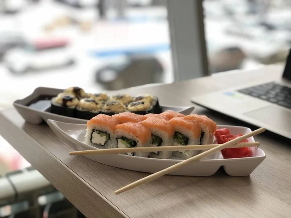 Luscious rolls Philadelphia on a table overlooking from the panoramic window the winter street, working atmosphere next to the laptop — Stock Photo, Image