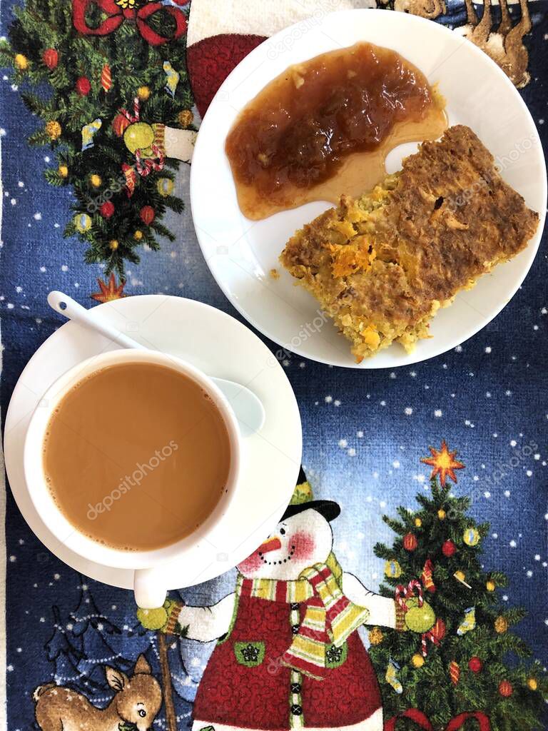 coffee and cake on white tableware on a festive tablecloth with the image of a snowman, Christmas tree and decorations. top view