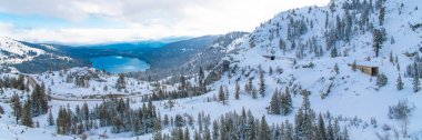The Donner lake under the snow in winter, in California, panorama, with tunnels in the mountain for the train clipart