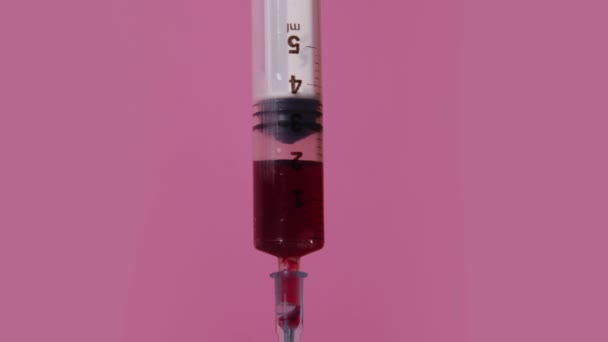 Syringe draws red liquid on a pink background — 图库视频影像