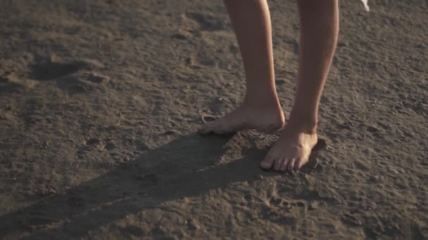 Девочка босиком поднимает ногу на песок — стоковое видео
