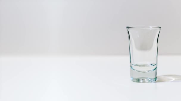Szkło jest wypełnione przezroczystym alkoholem na białym stole — Wideo stockowe
