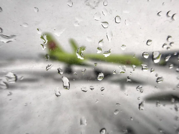 Rozostřená letadla se dívají na sklo s kapkami vody. Dešťové kapky na okně letadla u ranveje. — Stock fotografie
