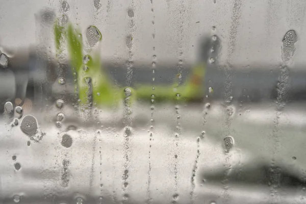 Aviões desfocados visualizam vidro com gotas de água. Gotas de chuva na janela do avião perto da pista . — Fotografia de Stock