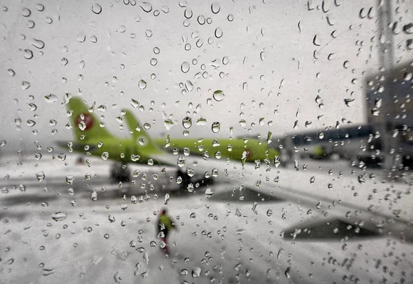 Samoloty bez skupienia oglądają szkło z kroplami wody. Krople deszczu na oknie samolotu przy pasie startowym. — Zdjęcie stockowe