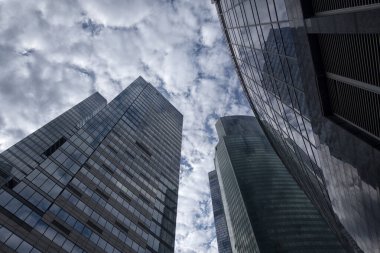 Aşağıdan gökdelenlerin manzarası. Gökdelenler mavi gökyüzüne karşı. Yüksek bina. Şehrin iş merkezi. Modern şehir mimarisi. Camdan ve betondan yapılmış evler.