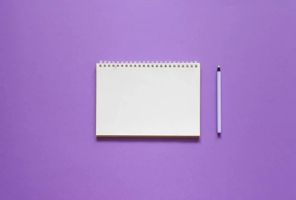 Mor zemin üzerinde spiral bir not defteri aç, defter ve kalem dokusal kağıt üzerinde uzan, düz konsept