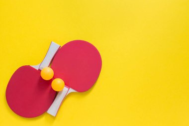 Sarı arka planda kırmızı tenis raketleri ve turuncu toplar. Masa tenisi için spor malzemeleri.