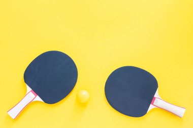 Sarı arka planda siyah tenis raketleri ve turuncu toplar. Masa tenisi için spor malzemeleri.