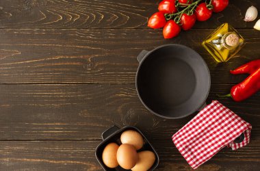 Kahverengi ahşap arka planda boş tava, sarımsaklı ve kırmızı biberli taze sulu domatesler, şişede zeytinyağı ve yumurta, kahvaltı, üst manzara, uzay malzemelerini kopyalamak.