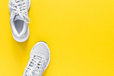 Sarı arka planda izole edilmiş beyaz spor ayakkabılar, yürüyüş ve spor için mevsimlik ayakkabılar, fotokopi alanı, üst manzara