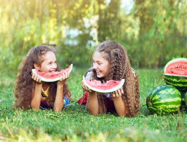 Happy friends on a picnic eating watermelon and smiling at each other lying on the grass. Having fun together. Concept summer time. Friendship.