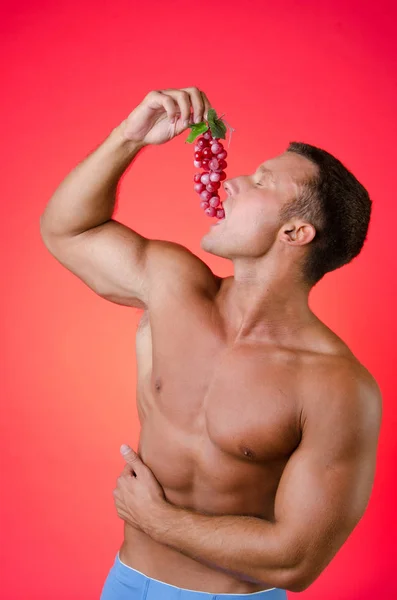 Σέξι άνδρας τρώγοντας σταφύλια. Κόκκινο φόντο. — Φωτογραφία Αρχείου