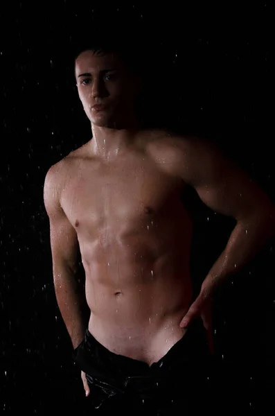 Sexy man in shower. Wet body and jeans. Black background.
