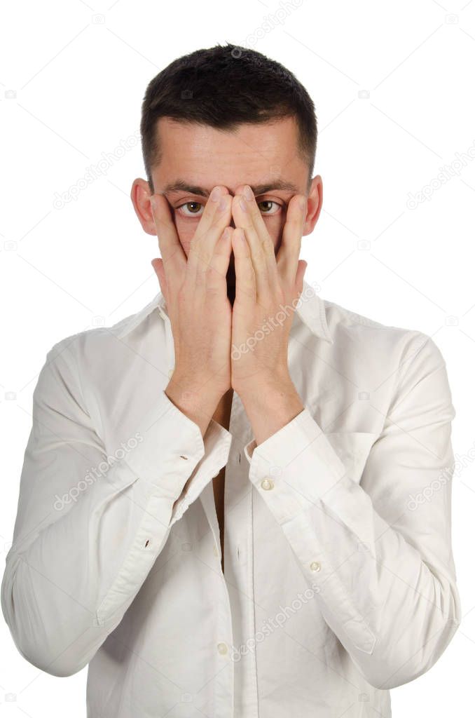 Young handsome guy covers his face with his hands. Handsome man closes his eyes with his hand and looks through his fingers