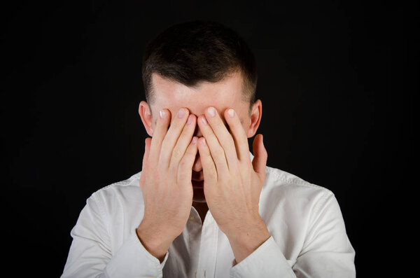 Young handsome guy covers his face with his hands. Business and stress. Office worker. Problems at work