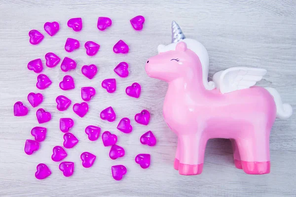 Cute pink unicorn on a wooden background. Lots of hearts. Valentines day.