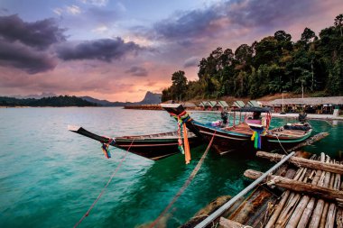 Güneş doğarken Tayland 'daki Khao Sok Ulusal Parkı' nda yüzen bungalovlar ve uzun kuyruklu tekneler..