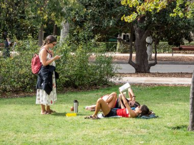 Madrid, İspanya, 9 Ekim 2019. Genç öğrenciler parkta yasalarla rahatlıyorlar. Çimenlerde konuşan üç kız..
