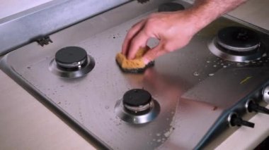 Bir adam kirli gaz sobasını sünger ve deterjanla yıkıyor.