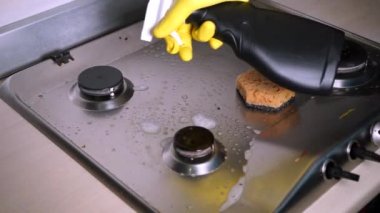 Lastik eldivendeki bir el, gaz sobasını yağ çıkarıcı ile tutar. Ev halkı kavramı.