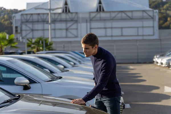 Joven hombre eligiendo un coche nuevo en una sala de exposición de vehículos o concesionario de automóviles — Foto de Stock