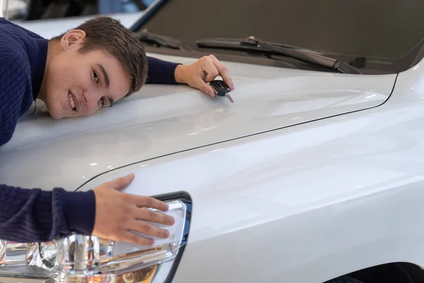 Un joven abrazando su nueva, grande y blanca camioneta, sonríe alegremente. Foto de un cliente feliz en la sala de exposición del coche — Foto de Stock