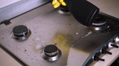 Koruyucu lastik eldivenli bir adam gaz sobasını yağ çıkarıcıyla yıkıyor.