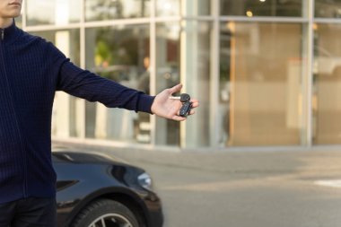 Bir erkek el arabanın arka planına karşı arabanın anahtarını tutuyor..