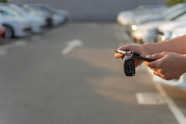 Auto business, car sale or rent concept. Hands of salesman with folder holds a car key over auto show background