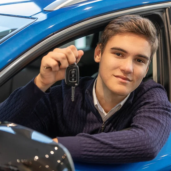 Feliz joven cliente sentado en coche nuevo y muestra la clave — Foto de Stock