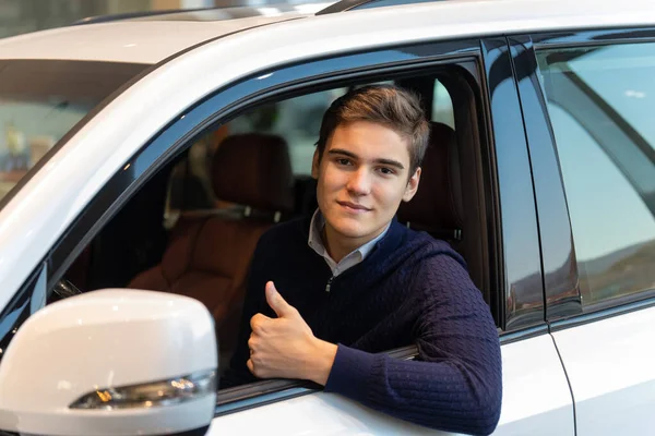 Un cliente felice, che compra un'auto nuova. Sta gesticolando verso l'alto, seduto dentro un'auto. . — Foto Stock